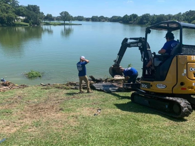 JChavez Flower Mound Tree Service 5 Crew operating a mini excavator at the edge of a pond